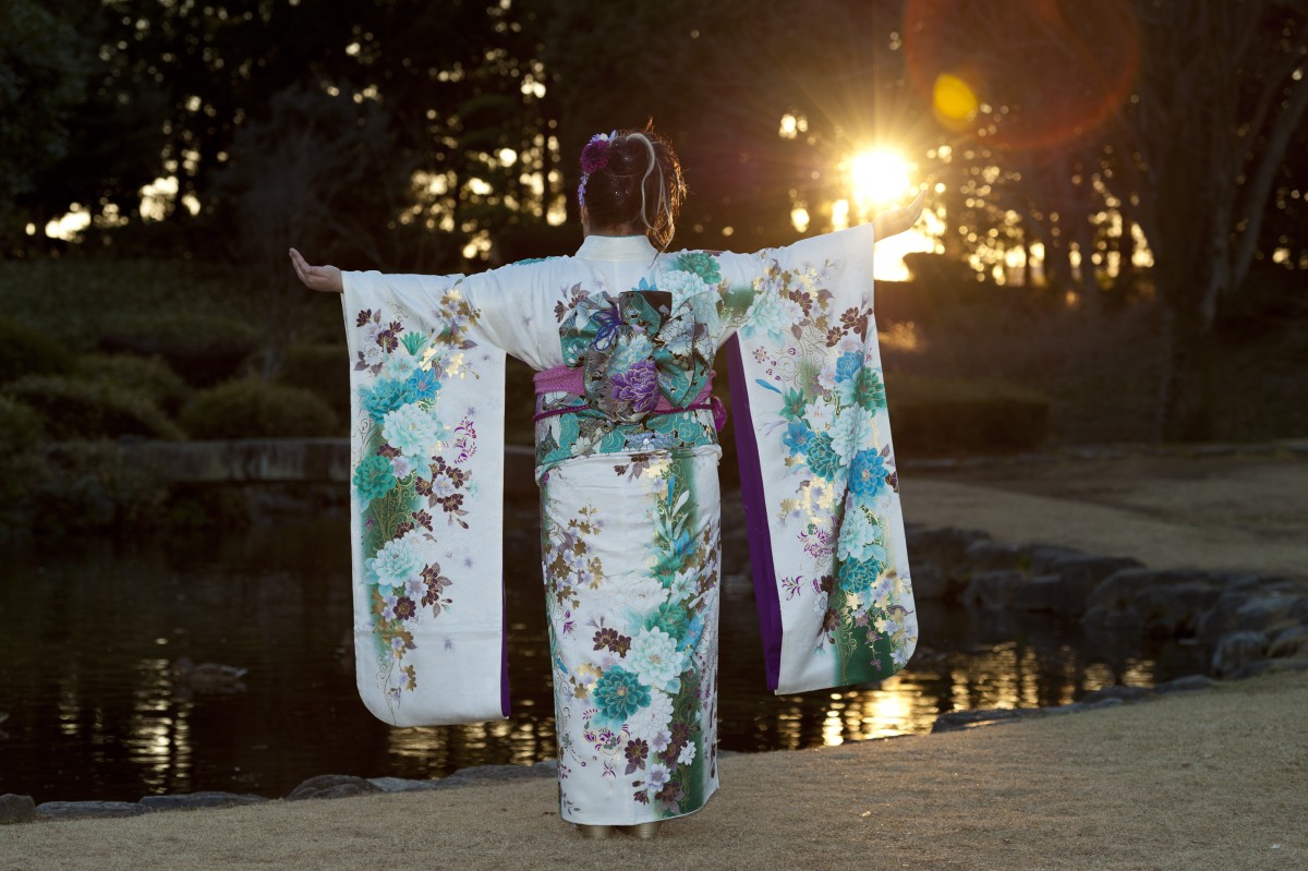 Adolescente japonesa usando um quimono tradicional com os braços esticados para trás e ao sol, comemorando o Dia da Maioridade em Fuji, Japão. Foto horizontal.