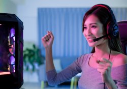 Jovem jogadora profissional asiática vence em jogo de vídeo online e comemora com as mãos para cima em casa.
