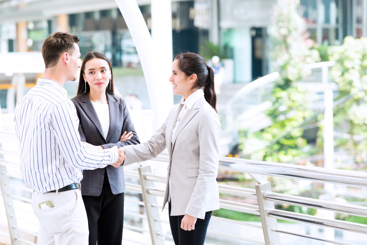 Konsep pertemuan bisnis yang ramah. Pertemuan bisnis di luar ruangan dengan dua wanita cantik dan pria kulit putih berbicara bersama membahas rencana bisnis. Diambil di luar ruangan dalam cahaya alami.