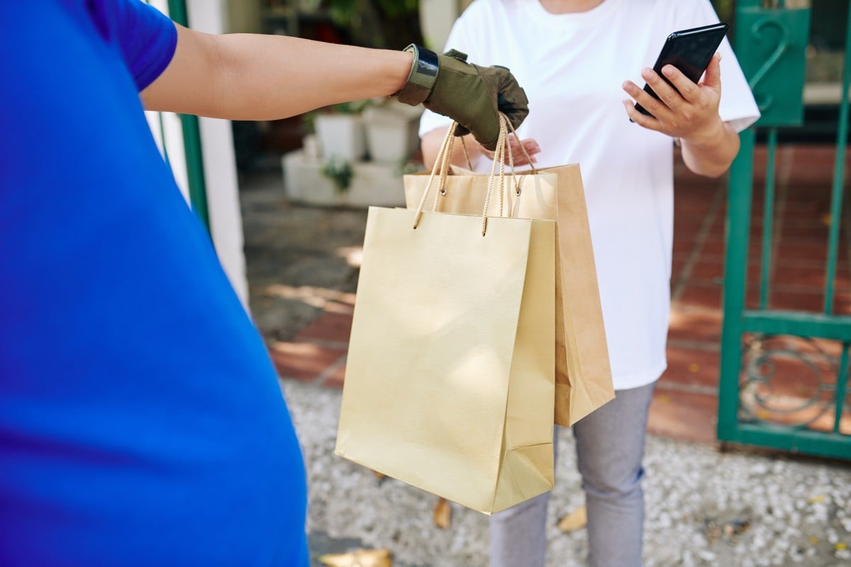 Repartidor entregando bolsas de papel a una clienta que deja propinas a través de una aplicación móvil