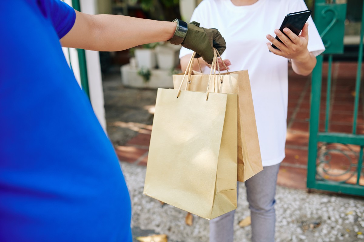 Fattorino che consegna sacchetti di carta alla cliente femminile che lascia mance tramite l'applicazione mobile