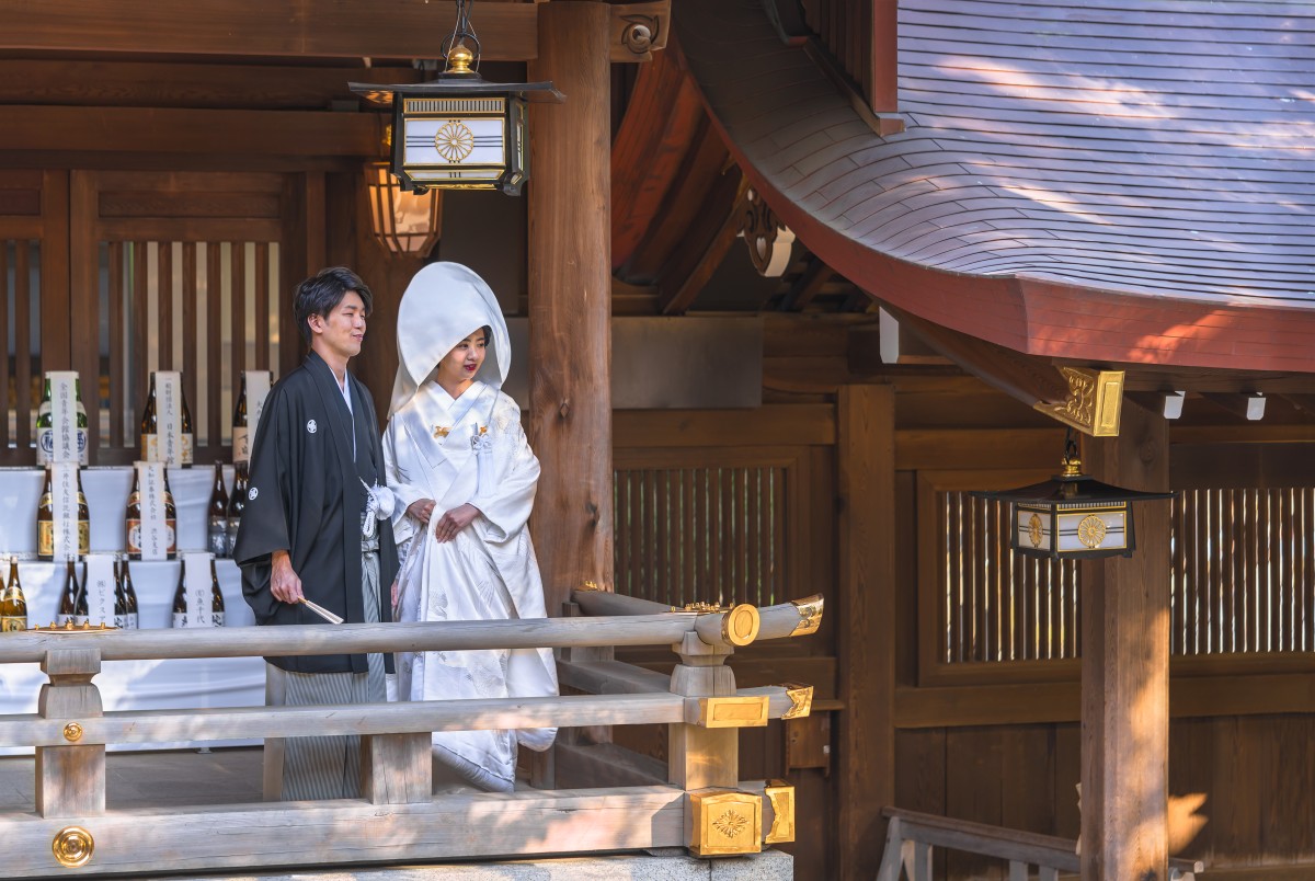 Pernikahan Shinto tradisional Jepang pasangan dalam kimono haori hitam dan shiromuku putih di dekat lentera yang dihias lambang kerajaan di Kuil Meiji.