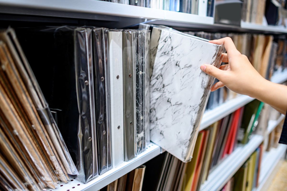 Mano masculina eligiendo una nueva carpeta de archivos de encuadernación con textura de mármol blanco de la estantería en la tienda de artículos de papelería. Concepto de compra de suministros de oficina