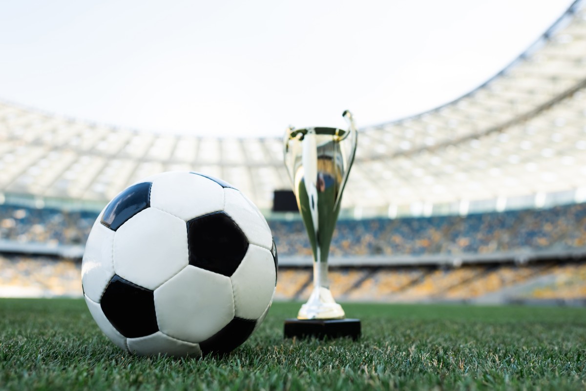 Soccer ball and trophy on grassy football pitch at stadium