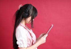 Das asiatische Mädchen im Teenageralter mit niedlicher japanischer Mitte steht auf dem roten Hintergrund.