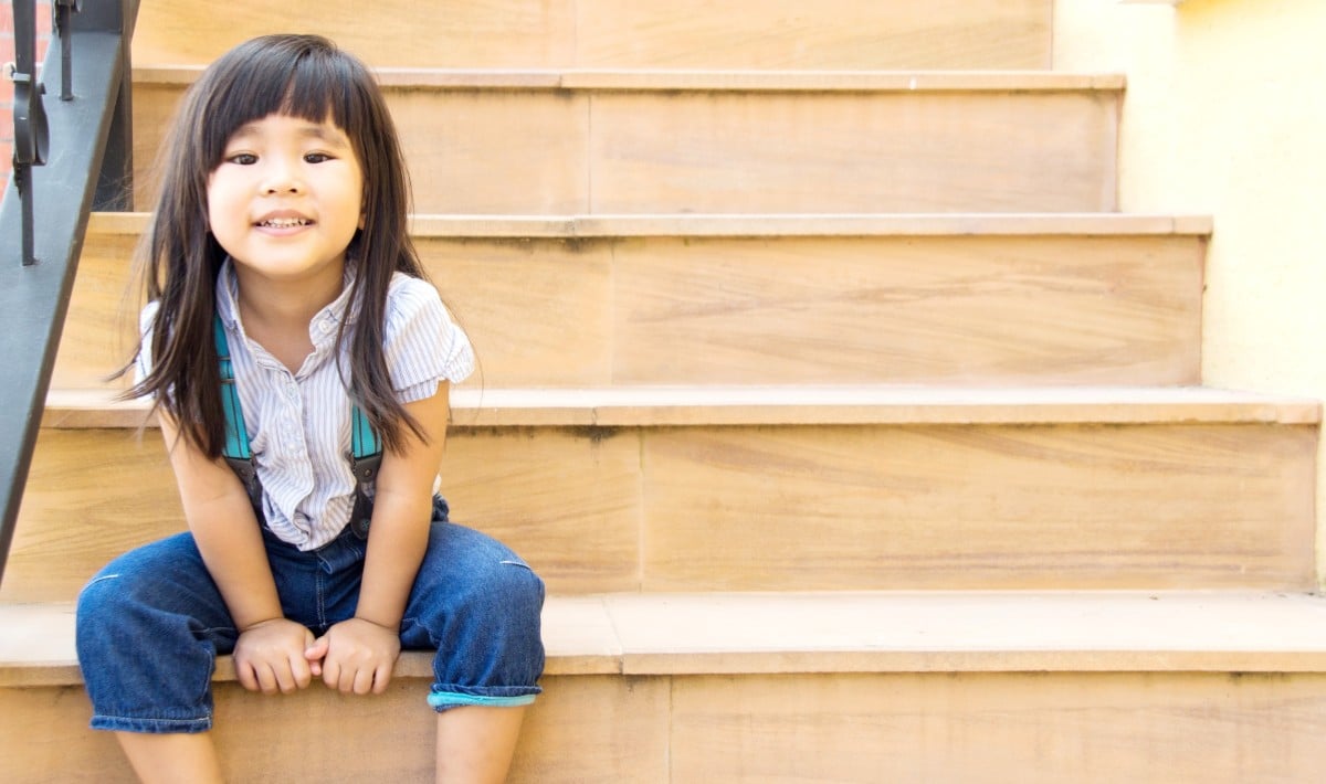 Menina asiática sorrindo sentada na escada amarela.