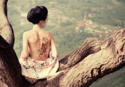 Donna con il tatuaggio del serpente sulla schiena sul ramo dell'albero