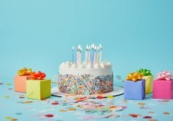 Delicious cake with candles, colorful gifts and confetti on blue background