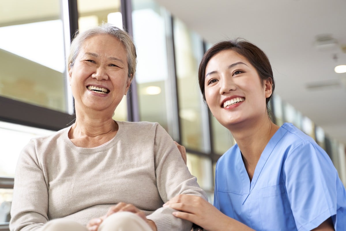Asiatische Seniorin und ihre Pflegekraft, die lächelnd in die Kamera schauen