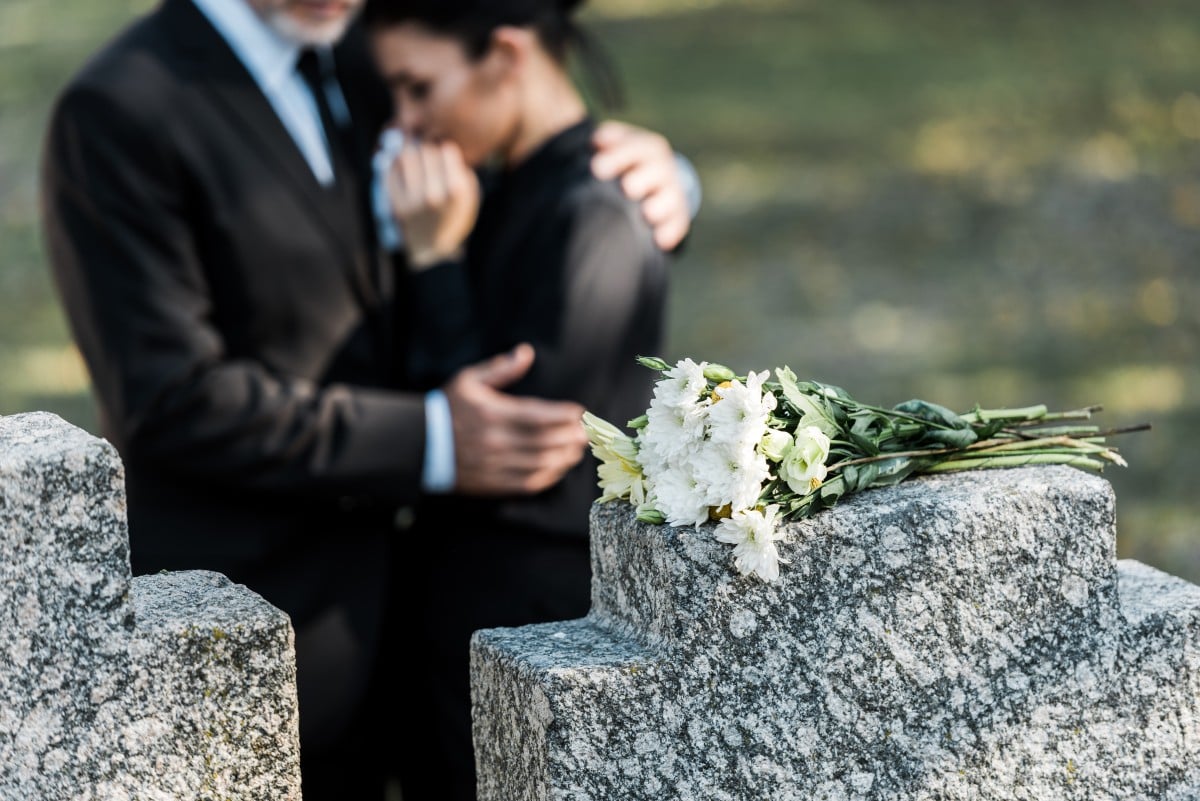 Selektiver Fokus des Blumenstraußes auf Grabstein in der Nähe eines Mannes, der eine Frau umarmt